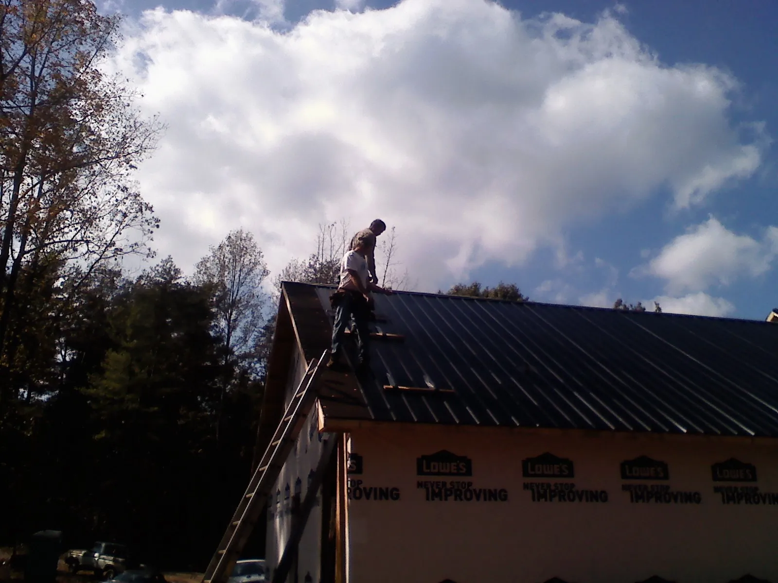 Roofer fastening dark metal panels high against a cloudy sky, from a Roof Inspection job in Randolph